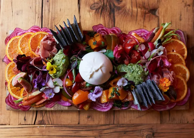 A colourful board of burrata, citrus, prosciutto, beets and flowers